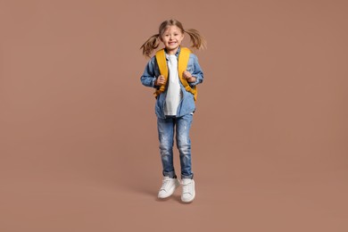 Photo of Happy schoolgirl with backpack jumping on brown background