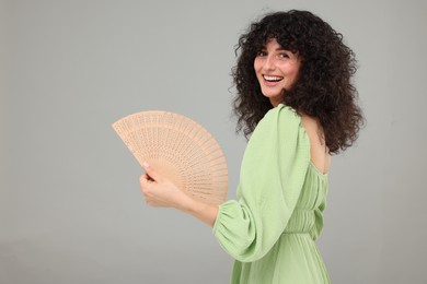 Photo of Happy woman holding hand fan on light grey background. Space for text