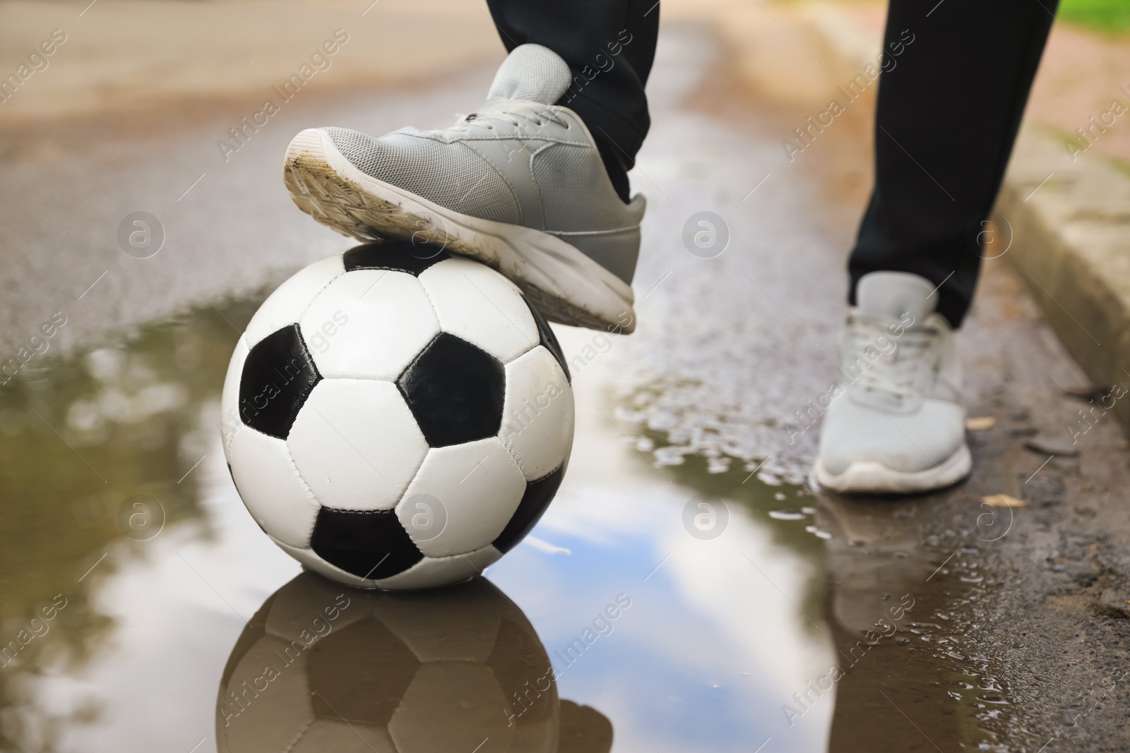 Photo of Man with soccer ball near puddle outdoors, closeup