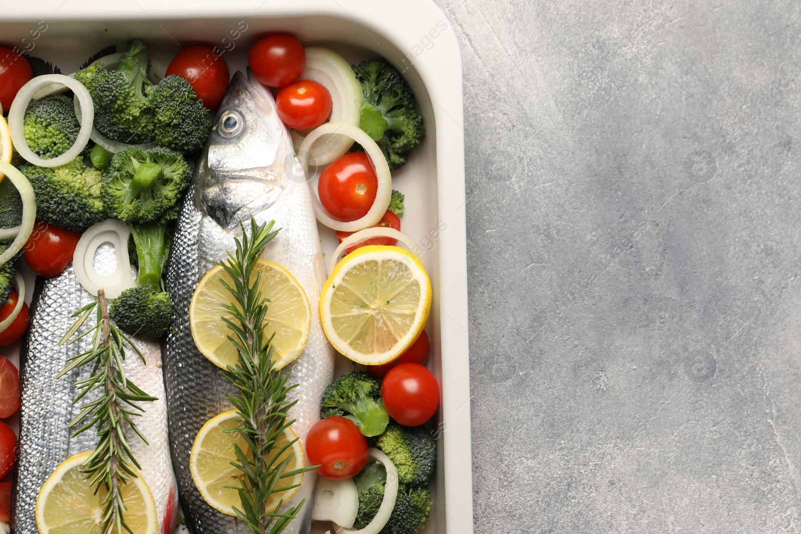 Photo of Raw fish with vegetables and lemon in baking dish on grey textured table, top view. Space for text