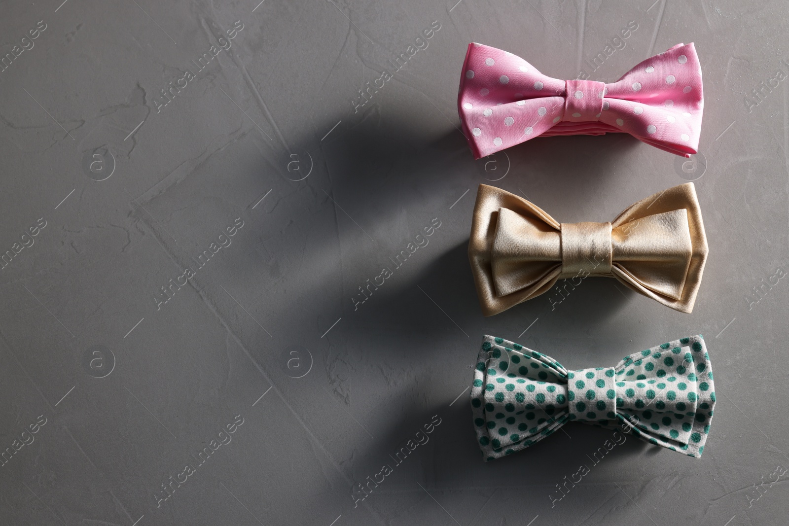 Photo of Stylish color bow ties on gray textured background, flat lay. Space for text