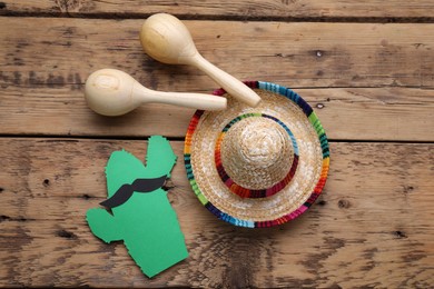 Maracas, paper cactus with mustache and sombrero hat on wooden table, flat lay. Musical instrument