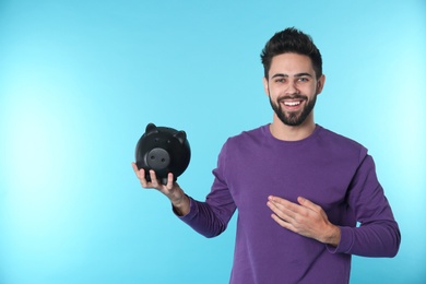 Happy young man with piggy bank and space for text on color background. Money saving