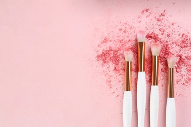 Makeup brushes and scattered eye shadow on pink background, flat lay. Space for text