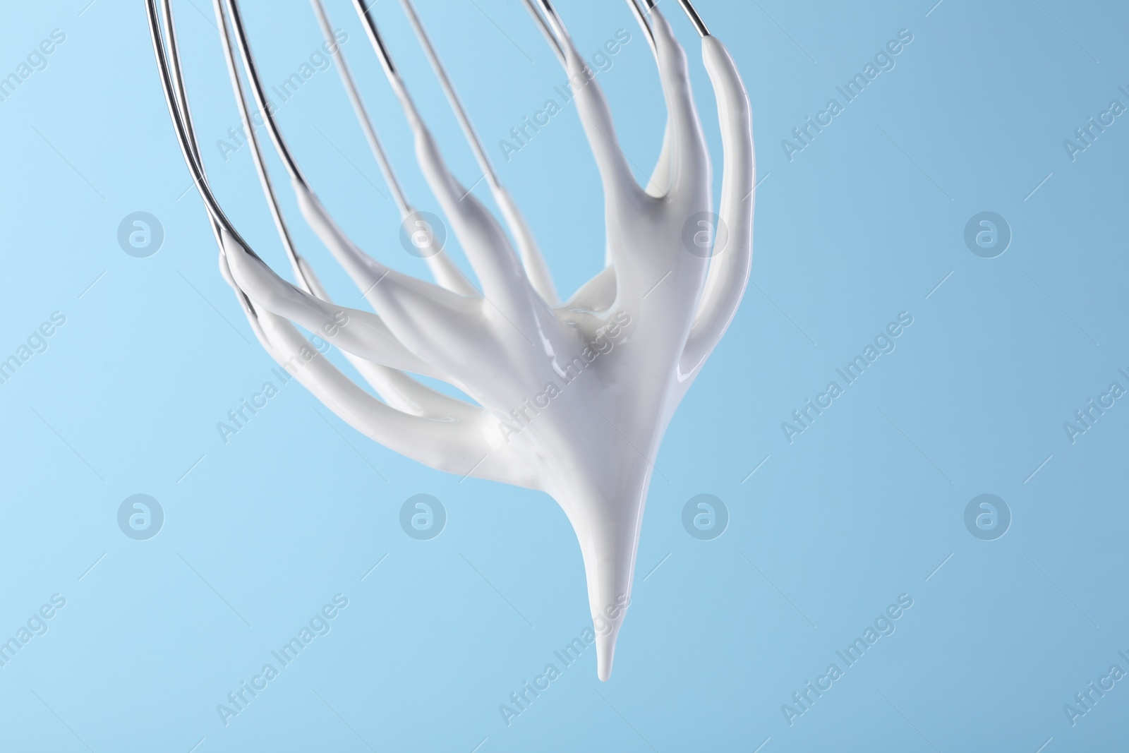 Photo of Whisk with whipped cream on light blue background, closeup