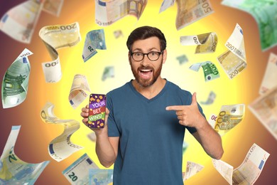 Image of Your Bet Wins! Emotional man pointing at smartphone under money shower against color background