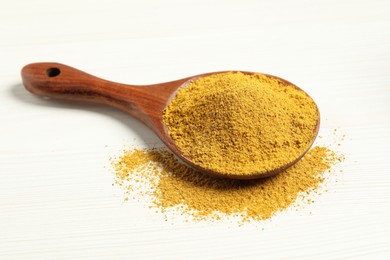 Photo of Curry powder in spoon on white wooden table