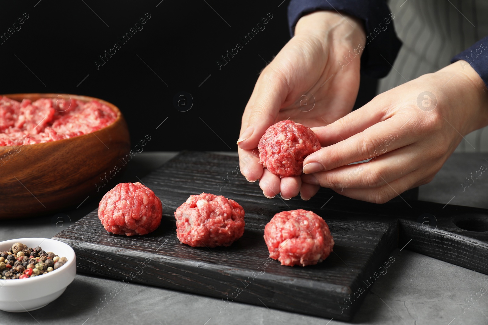 Photo of Woman making meatball from ground meat at grey table, closeup