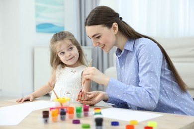 Mother and her little daughter painting with palms at home