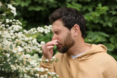 Photo of Man suffering from seasonal pollen allergy near blossoming tree on spring day