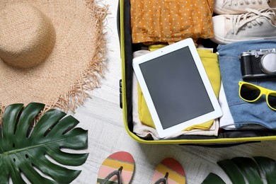 Photo of Packed suitcase with tablet and travel accessories on floor, flat lay. Summer vacation