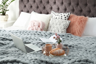 Tray with tasty breakfast, laptop and book on bed