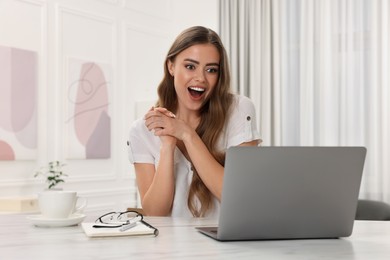 Surprised woman using laptop at white table in room