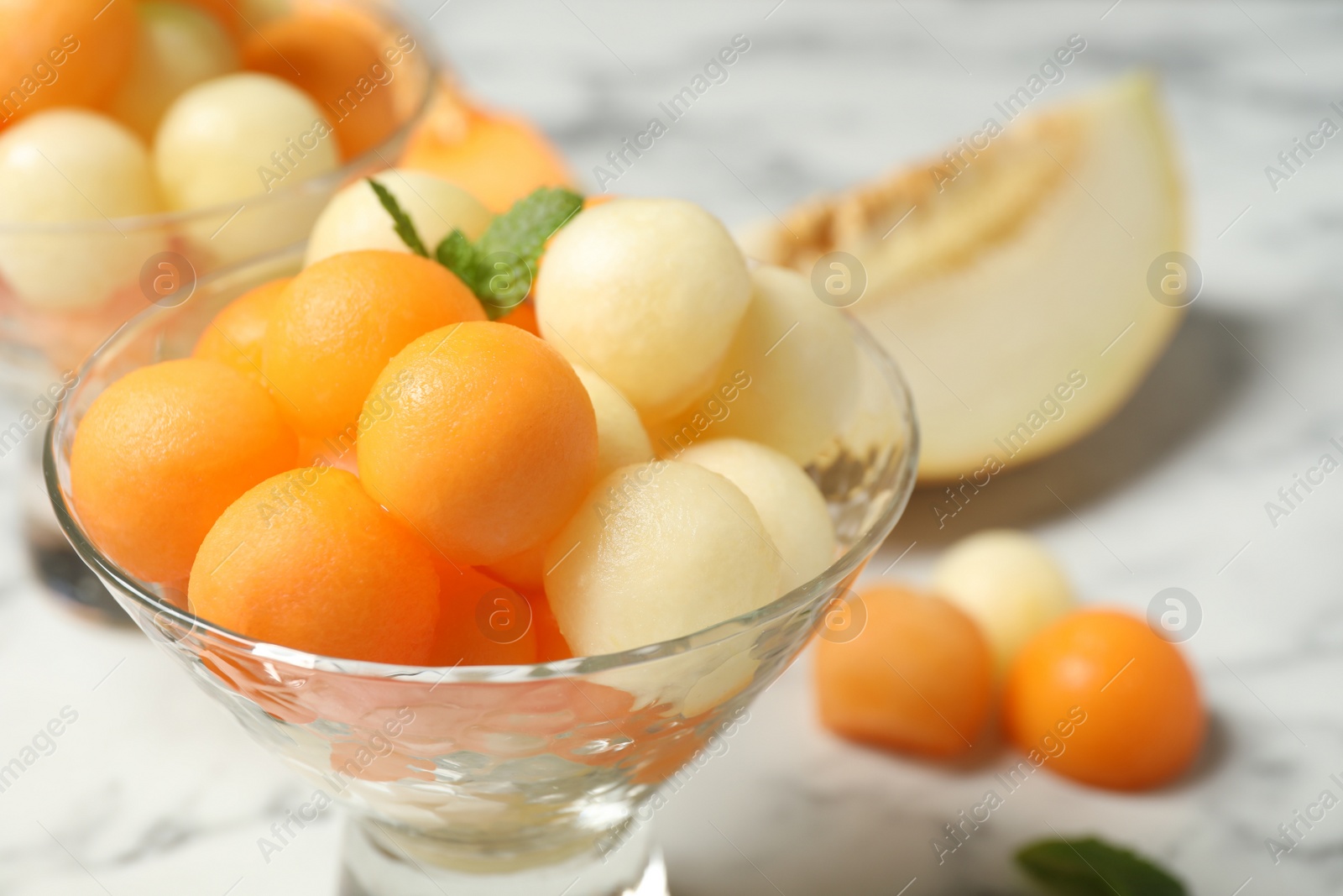 Photo of Melon balls and mint in glass on white table, closeup