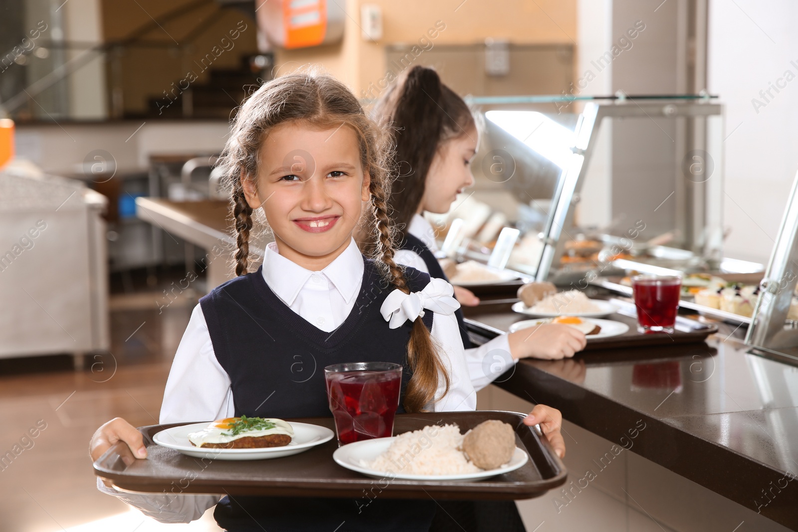 Photo of Cute girl holding tray with healthy food in school canteen