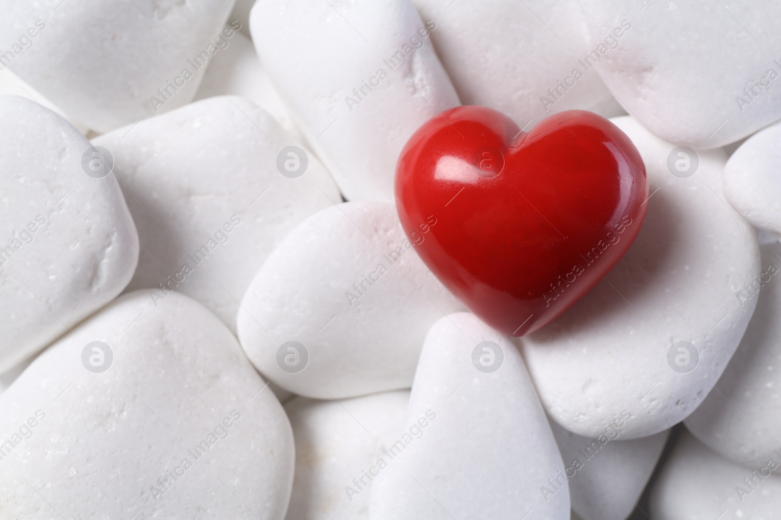 Photo of Decorative heart on white pebble stones, top view