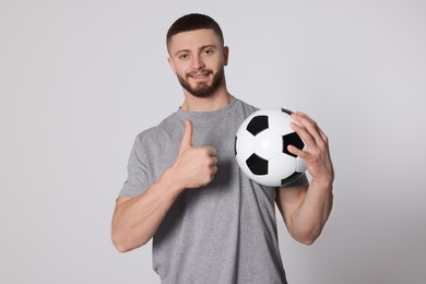 Photo of Athletic young man with soccer ball showing thumb up on light grey background