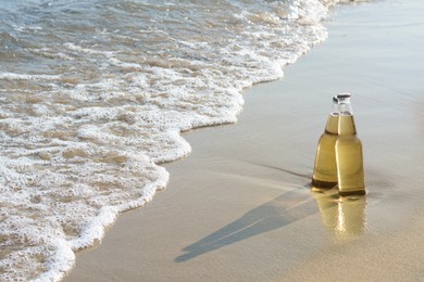 Bottles of cold beer on sandy beach near sea, space for text