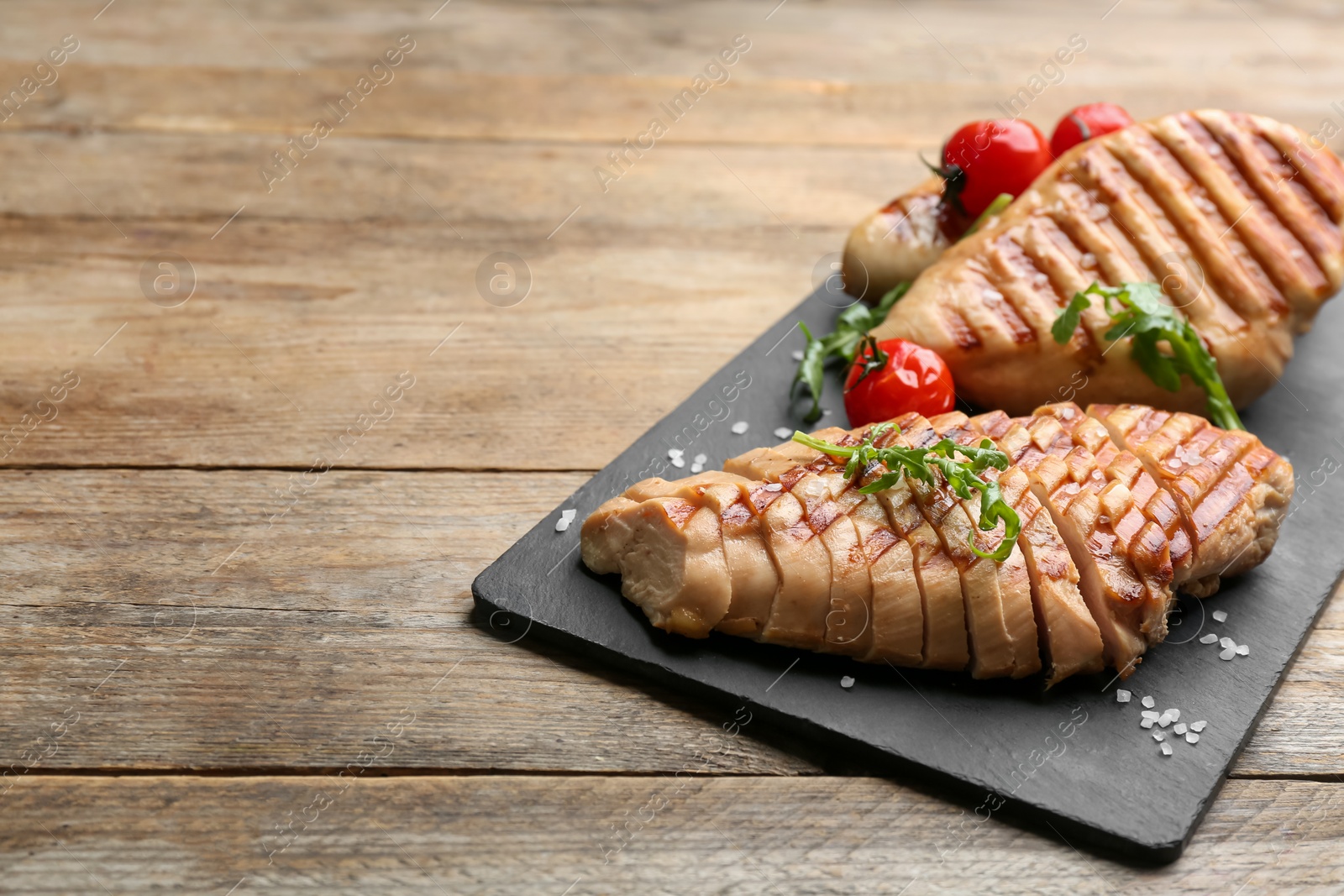 Photo of Tasty cut grilled chicken fillets with arugula on wooden table. Space for text