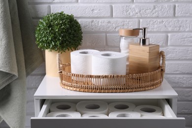 Photo of Toilet paper rolls, floral decor, dispenser and cotton pads on chest of drawers indoors