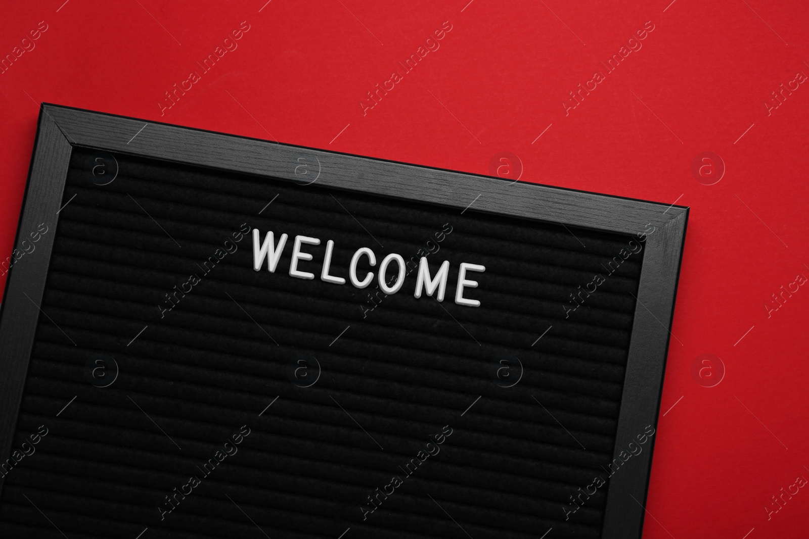 Photo of Black letter board with word Welcome on red background, top view