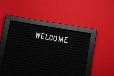 Black letter board with word Welcome on red background, top view