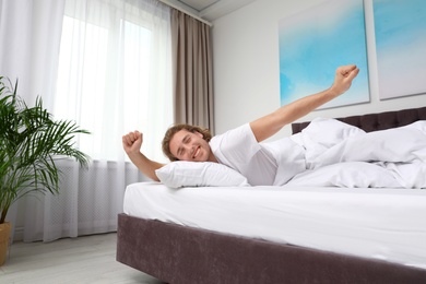 Photo of Sleepy young man stretching while lying under blanket in morning. Bedtime