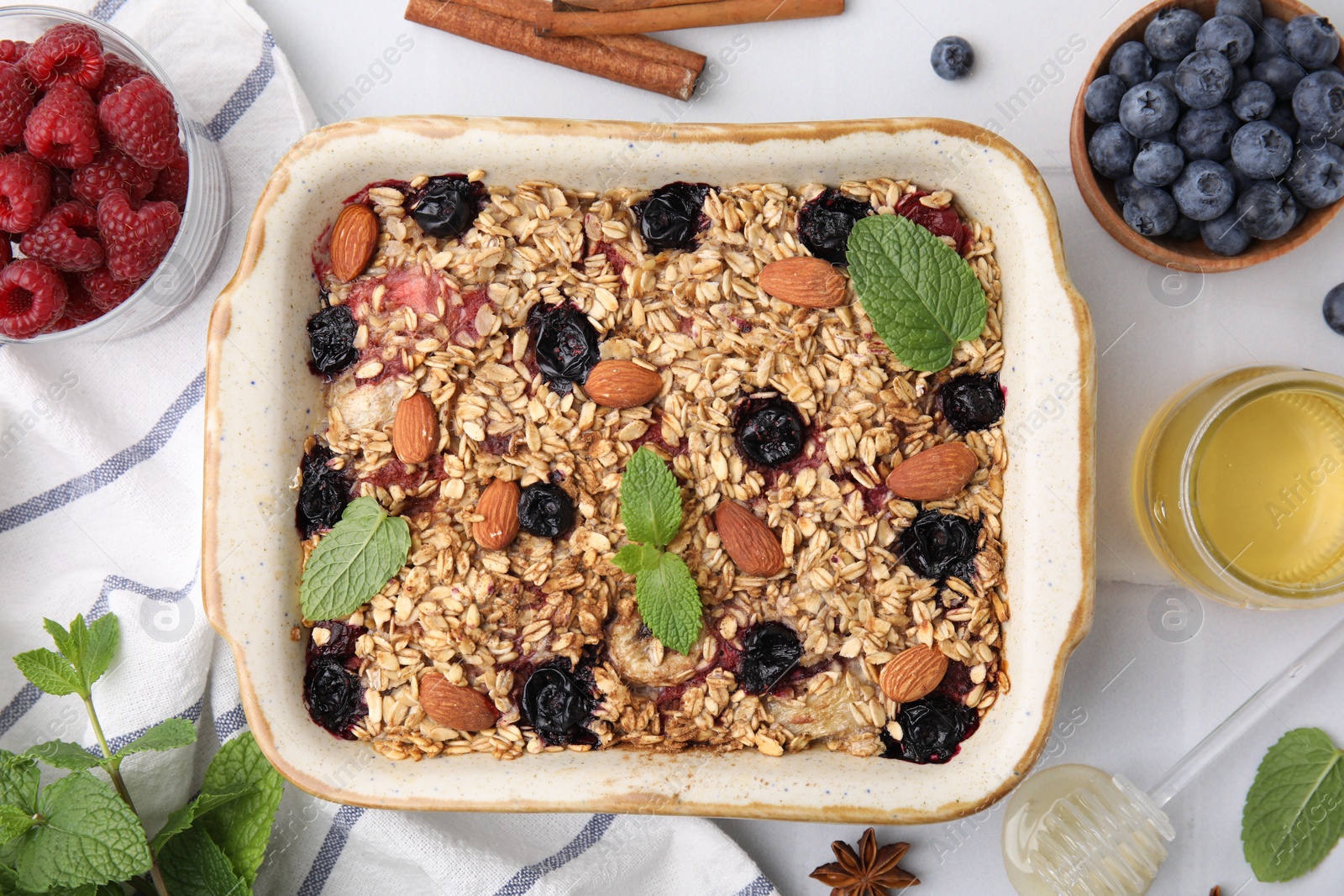Photo of Tasty baked oatmeal with berries, almonds and spices in baking tray on white tiled table, flat lay