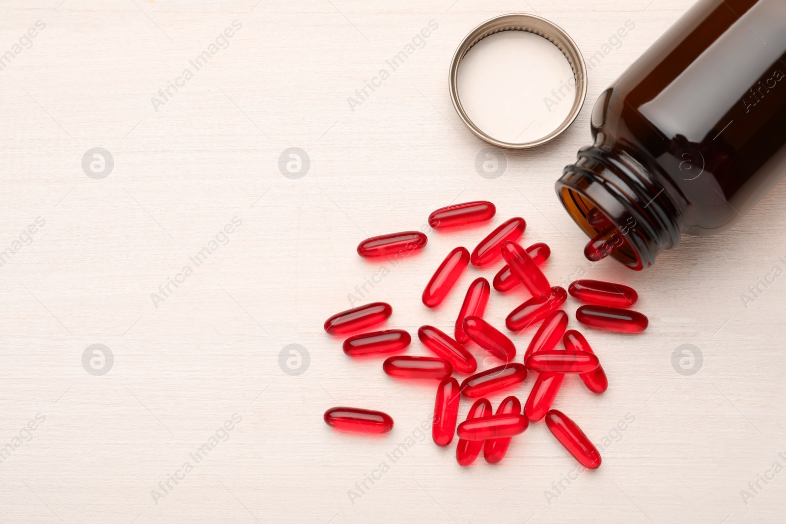 Photo of Overturned bottle with dietary supplement capsules on white wooden table, flat lay. Space for text