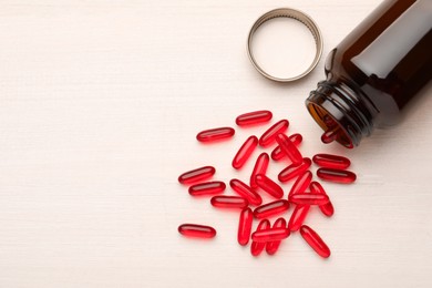 Photo of Overturned bottle with dietary supplement capsules on white wooden table, flat lay. Space for text