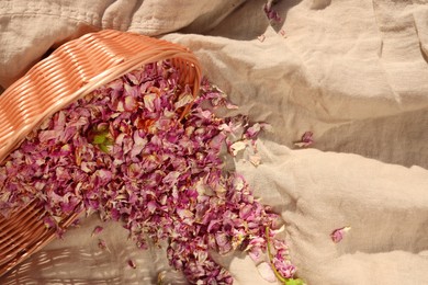 Photo of Overturned basket with dry tea rose petals on beige fabric