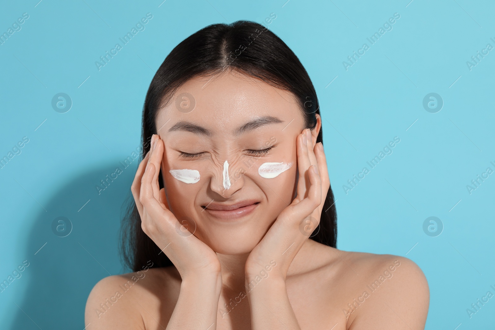 Photo of Beautiful young woman with sun protection cream on her face against light blue background