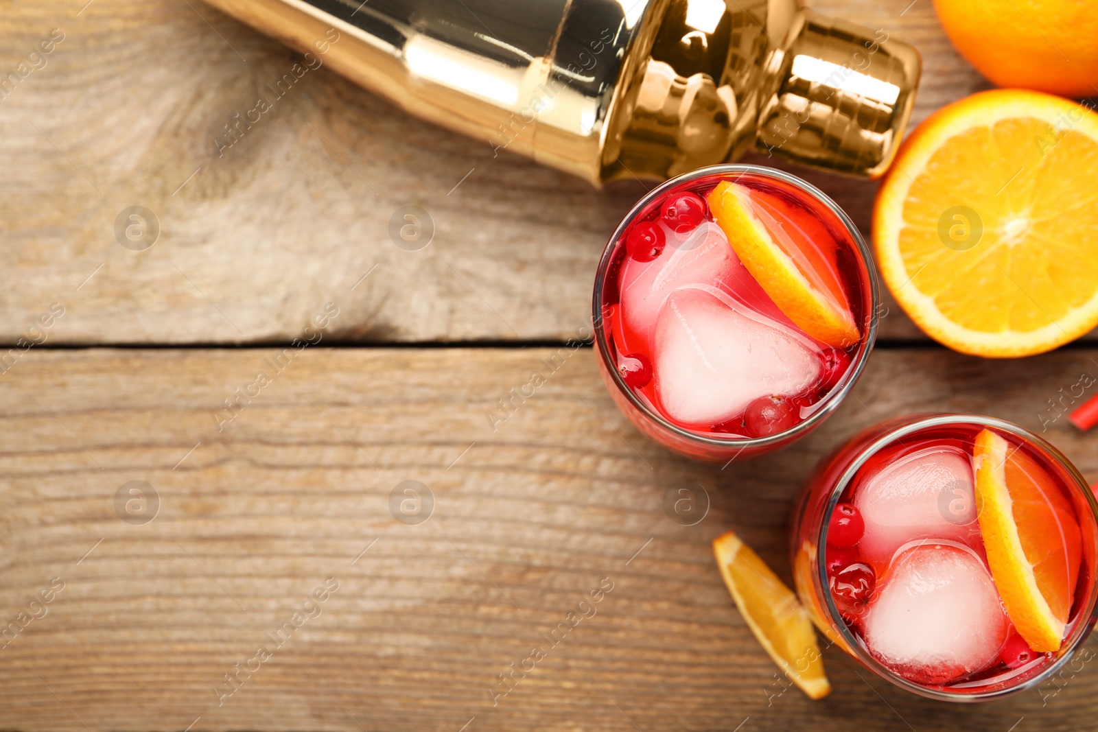 Photo of Tasty cranberry cocktail with ice cubes and orange in glasses on wooden table, flat lay. Space for text