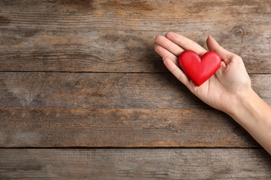 Woman holding red heart on wooden background, top view with space for text. Helping hand