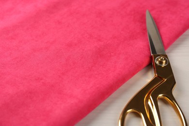 Scissors and pink fabric on light beige wooden table, closeup. Space for text
