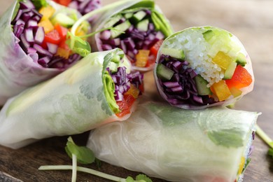 Delicious spring rolls wrapped in rice paper on wooden board, closeup