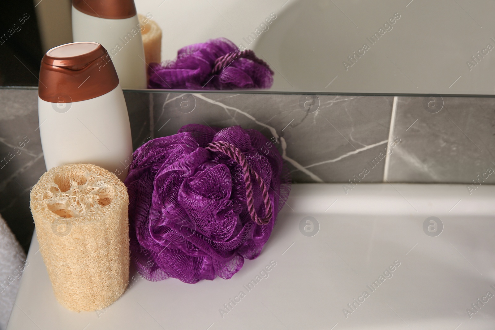 Photo of Purple shower puff, loofah sponge and bottle of body wash gel on sink in bathroom, space for text