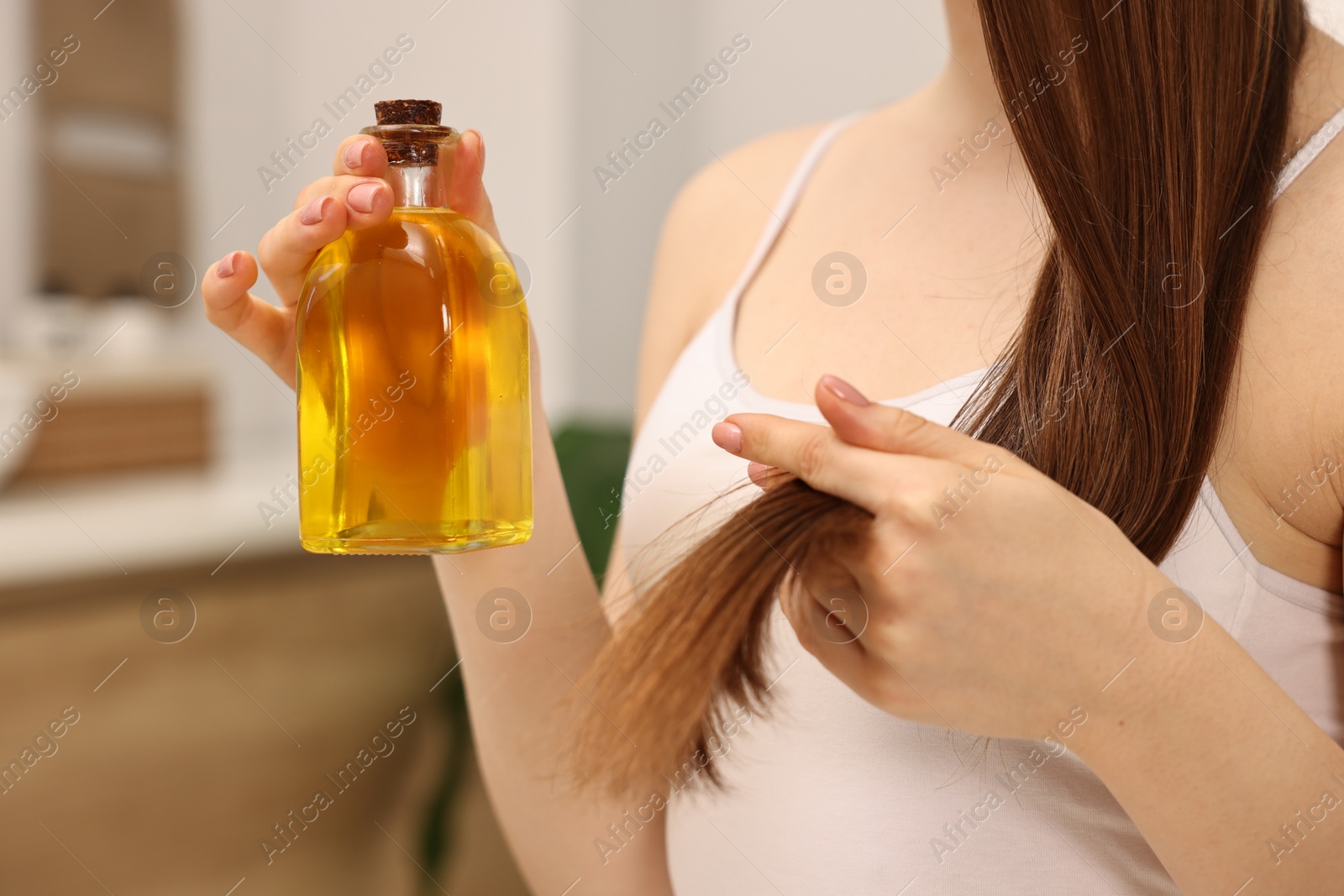 Photo of Natural hair mask. Woman holding bottle of oil at home, closeup