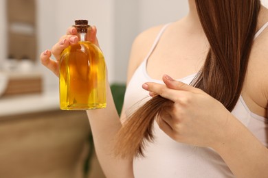 Photo of Natural hair mask. Woman holding bottle of oil at home, closeup