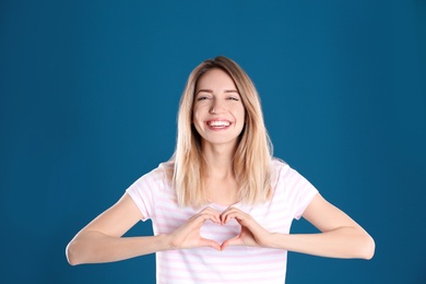 Portrait of pretty woman making heart with her hands on color background