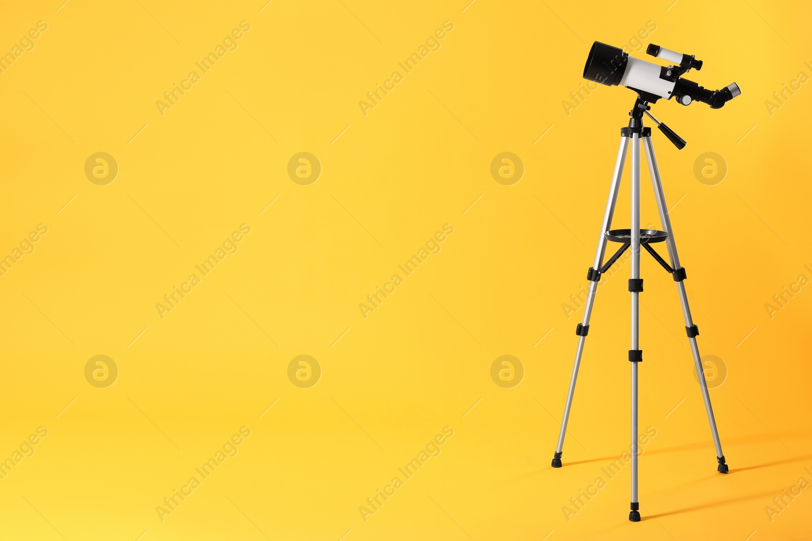 Photo of Tripod with modern telescope on yellow background. Space for text