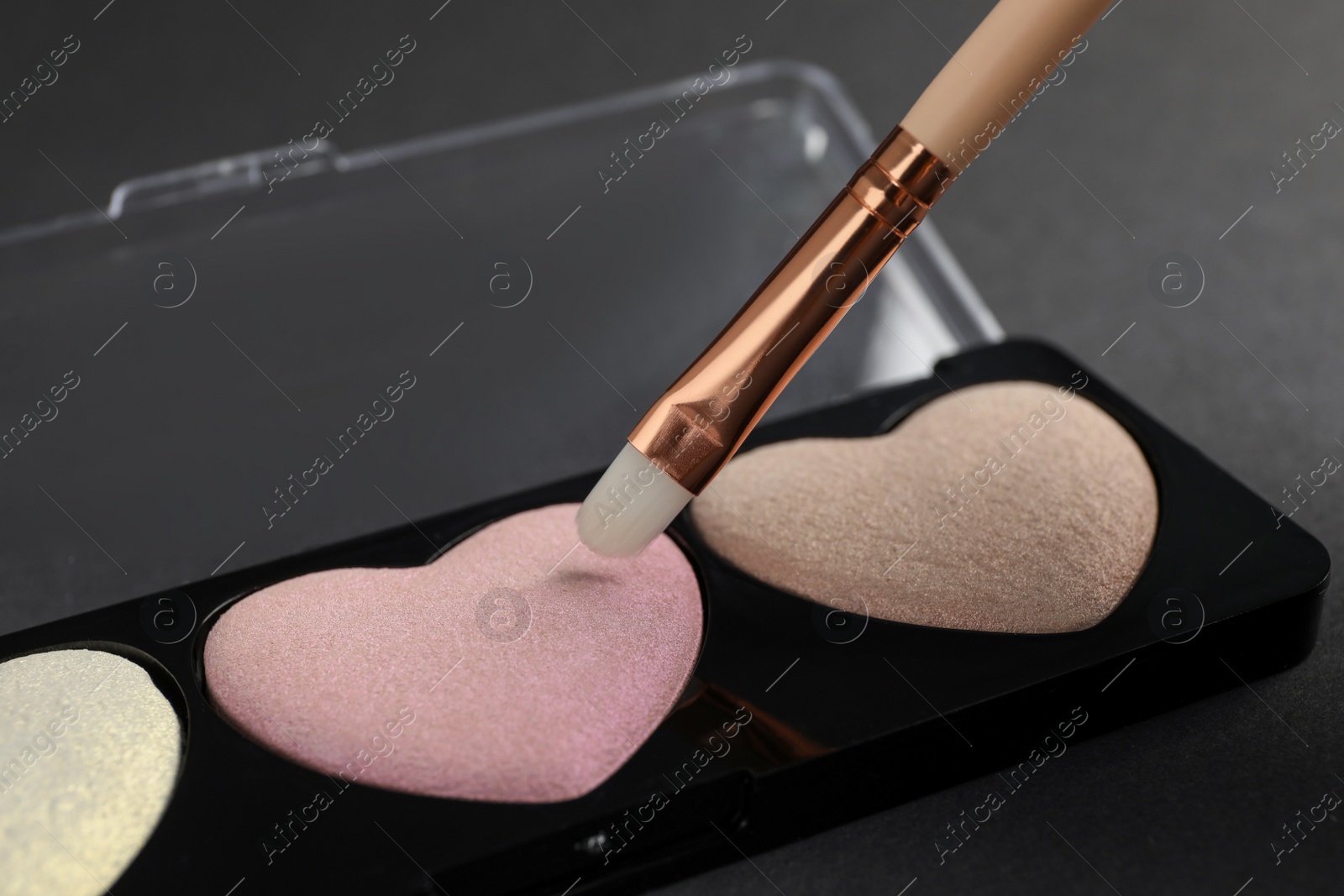 Photo of Palette of heart shaped eyeshadows with brush on dark background, closeup