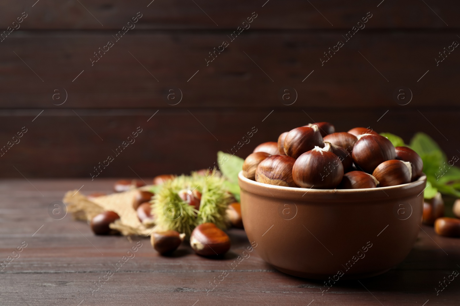 Photo of Fresh sweet edible chestnuts on brown wooden table. Space for text