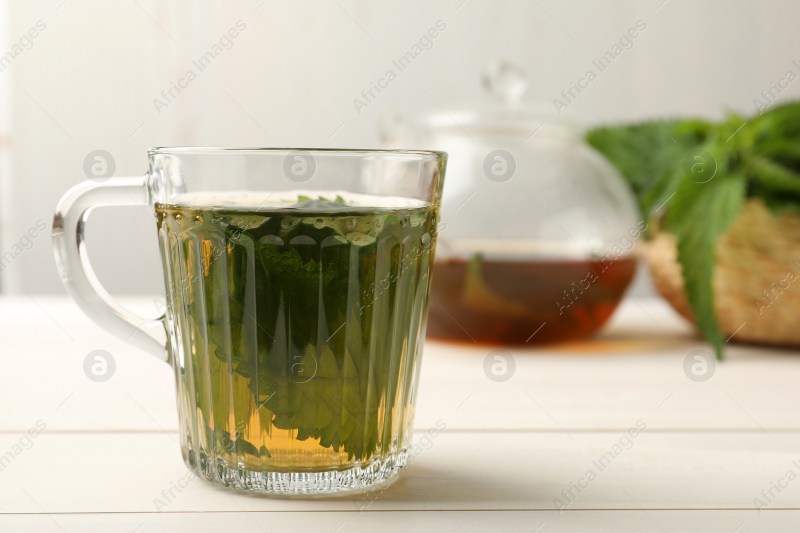 Photo of Glass cup of aromatic nettle tea on white wooden table, space for text