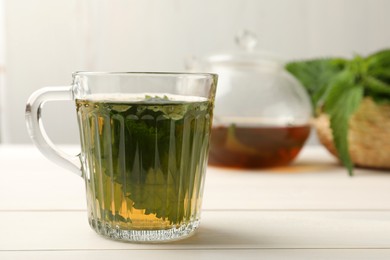 Glass cup of aromatic nettle tea on white wooden table, space for text