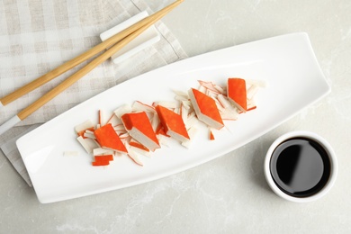Fresh delicious crab sticks with soy sauce served on marble table, flat lay