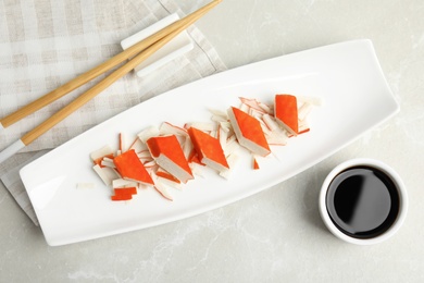 Photo of Fresh delicious crab sticks with soy sauce served on marble table, flat lay