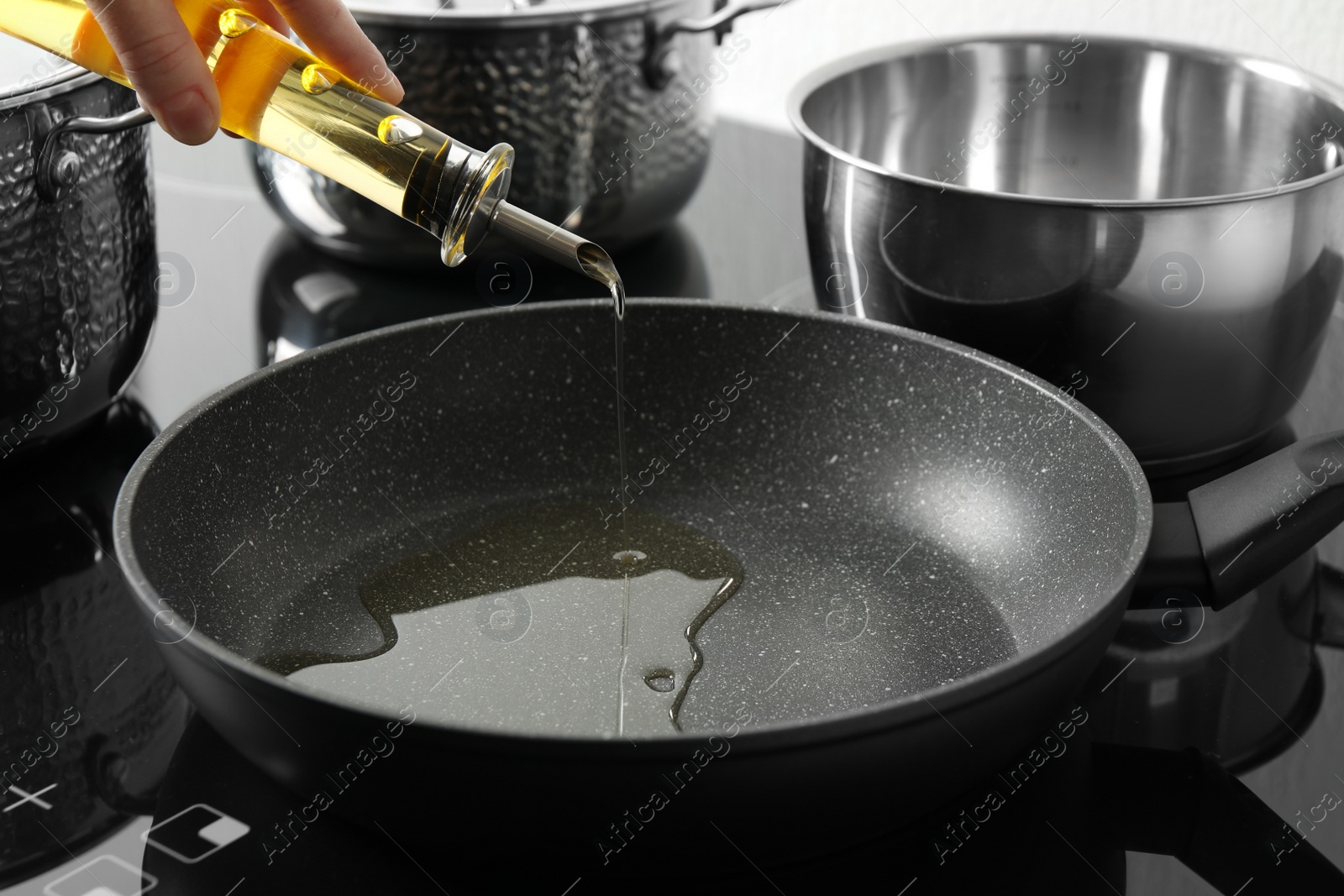 Photo of Woman pouring cooking oil from bottle into frying pan, closeup