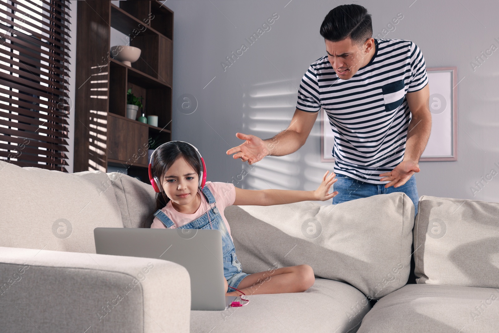 Photo of Internet addiction. Man scolding his daughter while she using laptop in living room