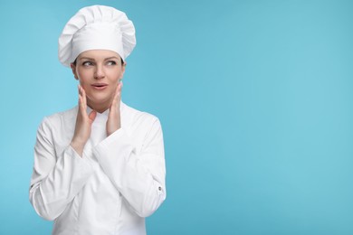 Happy woman chef in uniform on light blue background, space for text